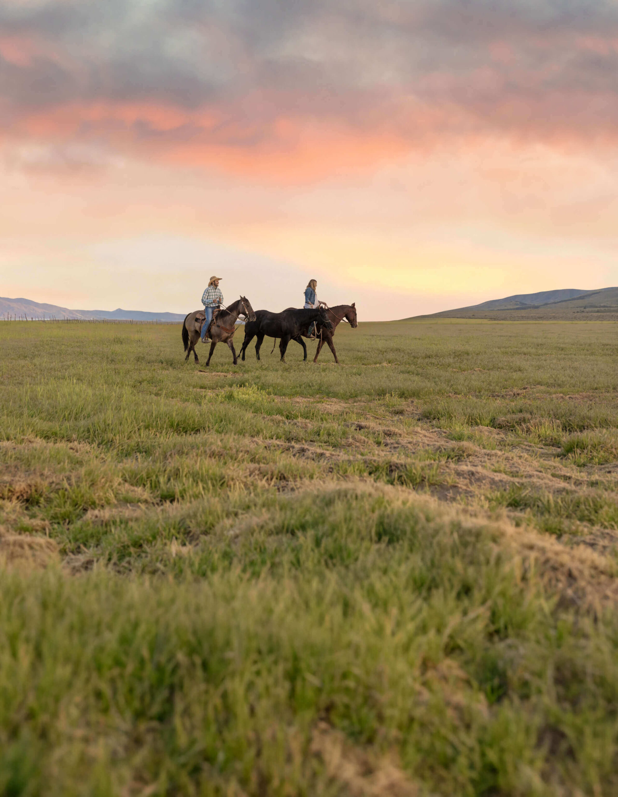Two riders cross open grassland beneath a sunset sky